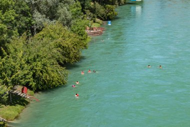 Bern, İsviçre - 30 Temmuz 2019: Güneşli yaz gününde Aare nehrinin panoramik manzarası. Kasaba sakinleri nehrin hızlı akışı boyunca şişme botlarda güneşlenip rafting yapıyorlar.