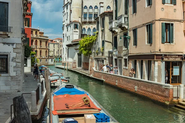 VENECIA, ITALIA - 02 de agosto de 2019: Uno de los miles de rincones acogedores de Venecia en un día claro y soleado. Locales y turistas paseando por los edificios históricos y canales con embarcaciones amarradas — Foto de Stock