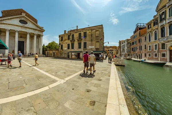 VENECIA, ITALIA - 02 de agosto de 2019: Uno de los miles de rincones acogedores de Venecia en un día claro y soleado. Locales y turistas paseando por los edificios históricos y canales con embarcaciones amarradas — Foto de Stock