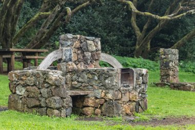 Huge stone barbecue for cooking meat, seafood during the holidays. Benches, a wooden table for food, a tap with drinking water and a unique relict forest in the background. Laguna Grande, La Gomera