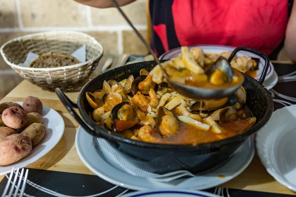 On the dining table is a hot pan with Seafood stew - Zarzuela. horizontal view, closeup. Selective center focus and blurred foreground