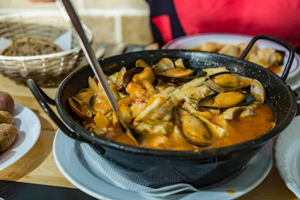 On the dining table is a hot pan with Seafood stew - Zarzuela. horizontal view, closeup. Selective center focus and blurred foreground