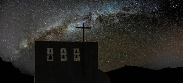 Σταυρός στην εκκλησία πάνω από καθαρό νυχτερινό ουρανό και φωτεινό Γαλαξία μας. Έξι καμπάνες διαφορετικού μεγέθους στην κορυφή. Κορυφές των ψηλών βουνών στο βάθος — Φωτογραφία Αρχείου