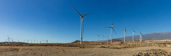 Super wide panorama of Wind power stations. A row of turbines near the seashore. Wind farm eco field. Eolic park with blue sky in background. Green, ecological and power energy generation concept.