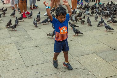 St. Mark Meydanı, VENICE, İtalya - 02 Ağustos 2019: sıcak güneşli bir yaz günü. Çok sayıda turist şehir güvercinleriyle fotoğraflanıyor. Çocuklar oyun oynar ve kuşlarla oynamaya çalışır..