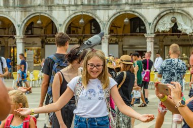 St. Mark Meydanı, VENICE, İtalya - 02 Ağustos 2019: sıcak güneşli bir yaz günü. Çok sayıda turist şehir güvercinleriyle fotoğraflanıyor. Çocuklar oyun oynar ve kuşlarla oynamaya çalışır..