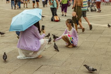 St. Mark Meydanı, VENICE, İtalya - 02 Ağustos 2019: sıcak güneşli bir yaz günü. Çok sayıda turist şehir güvercinleriyle fotoğraflanıyor. Çocuklar oyun oynar ve kuşlarla oynamaya çalışır..