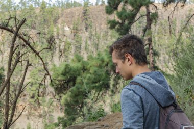 Sırt çantalı genç bir adam Tenerife 'nin batı yakasında bir rota boyunca seyahat ediyor. Dağ yolunda yürüyüş yapmak. Etrafı çam ağaçları ve lav kayaları ile çevrili. Kanarya Adaları.