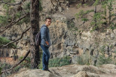 Sırt çantalı genç bir adam Tenerife 'nin batı yakasında bir rota boyunca seyahat ediyor. Dağ yolunda yürüyüş yapmak. Etrafı çam ağaçları ve lav kayaları ile çevrili. Kanarya Adaları.