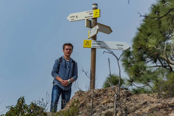 A young man with a backpack travels along a route in the west side of Tenerife. Hiking by the mountain trail surrounded by endemic vegetation pine tree forest and fields of lava rocks. Canary Islands.
