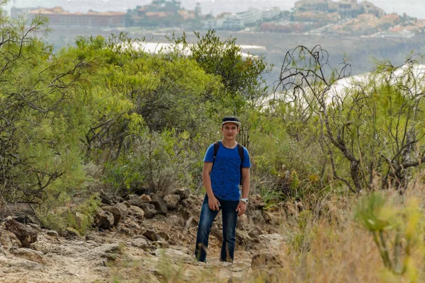 A young man with a backpack travels along a route in the west side of Tenerife. Hiking by the mountain trail surrounded by endemic vegetation and fields of lava rocks. Canary Islands, Spain.