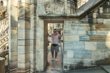 Milan, İtalya - 1 Ağustos 2019. Kemerinde çanta olan güneş gözlüklü genç bir adam İtalya 'daki Milan Katedrali' nin çatısında duruyor. Seçici odak portresi.