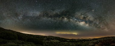 Milky Way in the spring sky above Teide National Park near Observatory. Jupiter is sparkling surrounded by star clusters and nebulae. Night lights over the coast and Gran Canaria in the background. clipart