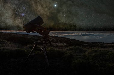 Gümüş bulutların üzerinde gece gökyüzü. Teleskop ilkbaharda Samanyolu 'nu izliyor. Gözlemevi yakınlarındaki Teide Ulusal Parkı' ndan görülüyor. Jüpiter yıldız kümeleri ve nebulalar tarafından kuşatılmıştır..