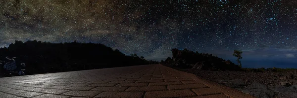 Büyük parlak bir ayın gümüş ışığında, bir dağ yolunda yıldızlı gece gökyüzü. Donmuş lav akıntısı üzerinde yapayalnız bir çam, yıldız kümeleri ve nebula dağılımının arka planına karşı..