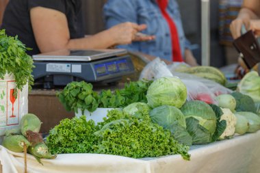 Şenlikli tarım pazarı. Taze sebzeli tezgahlardan biri kabak, lahana, salata, kişniş ve daha fazlası. Tezgahın sahibi müşterilere servis yapar..
