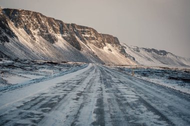 Kış yolda kar kar fırtınası. Parçalı yolun karşısında. Zor koşullar kış sezonunda İzlanda'sürüş. Güneşli ama rüzgarlı gün, tipik İzlanda yol sorunları. İzlanda Emanet sürüş.