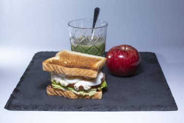 Yumurtalı sebzeli sandviç, marul, domates ve meyve suyu. Yanında bir elma da var. Hapis için sağlıklı yiyecekler.