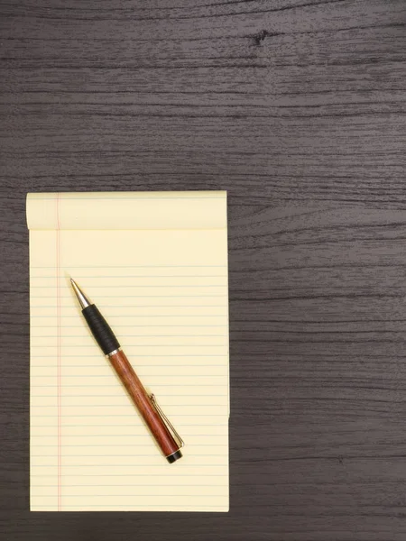 Drewniane biurko, żółty Notatnik, długopis — Zdjęcie stockowe