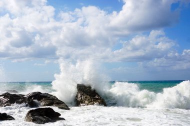 Deniz dalgaları kayalara çarpıp su damlacıkları yağmuru yaratıyor.