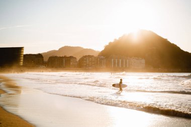Surfer enters to the water on Zurriola Beach in San Sebastian during sunset clipart