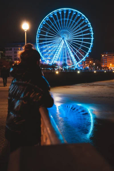 Ung flicka bär en gryning jacka titta på stora upplysta pariserhjul i San Sebastian — Stockfoto