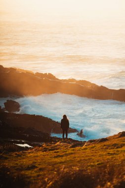 Yalnız kız büyük dalgaların kayalara çarpmasını izliyor.