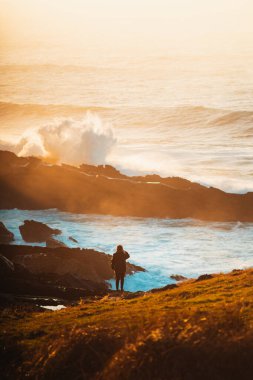 Yalnız kız büyük dalgaların kayalara çarpmasını izliyor.