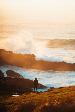 Yalnız kız büyük dalgaların kayalara çarpmasını izliyor.