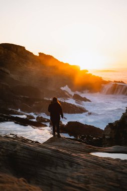 Dalgalar kıyı şeridine çarparken gün batımını izleyen bir kız.