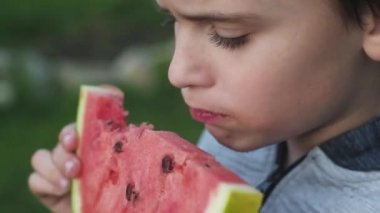 hungry boy happily eats a thick piece of juicy ripe red watermelon. Natural food in nature. Juicy red watermelon. Healthy diet. Summer vegetables and fruits. close up.