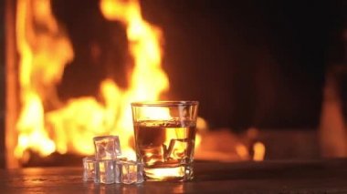 Eğlence partisi için buzlu viski, parlak kıvılcımlar ve şöminede yanan alevlere karşı. Çerçevenin ortasında buz küpleriyle masada bir bardak bayat içki..