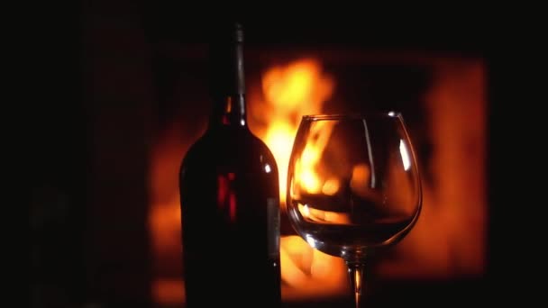 燃える炎を背景に暖炉の前のテーブルの上に空のガラスと赤ワインのボトルが立っています 友達の輪の中でクリスマス休暇 暖かい暖炉のそばで休もう — ストック動画