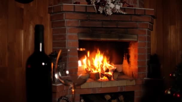 láhev vína a čiré víno sklenice stojí na stole na pozadí hořícího ohně vánočního krbu. Nový rok útulné dovolené s rodinou a přáteli. Panorama natáčení slavnostního interiéru.