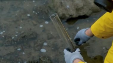 Çevre bilimci şehir nehrinden bir tüp su alıyor ve test tüpünün içeriğini inceliyor. Nehirdeki su kirliliğinin analizi. Çevrenin bakımı ve korunması. Kapat.