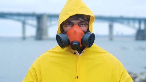 一个身穿红色呼吸器和黄色雨衣的环境专家愤怒地盯着相机的画像 专家站在城市河畔的桥的背景上 环境的养护和养护 — 图库视频影像