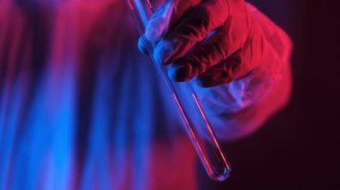 Önlüklü neon mavi ışık kullanan bilim adamı test tüpü tutuyor ve içine beyaz kristal tozu döküyor. Araştırmacı kimyasalı serpiyor. Kimyasal ve Biyolojik deneyler. Yeni bir uyuşturucunun geliştirilmesi.