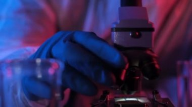 Neon ışığıyla bilimsel ve teknik laboratuvarda çalışan araştırmacı, ultra modern bilgisayar işlemcisini mikroskop ile inceliyor. Bilimsel endüstriyel araştırma. Modern teknolojik gelecek kavramı