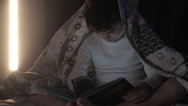 Chłopak Przykrył Się Kocem Wieczorem Czytając Książkę Sypialni Łóżku Oświetlenie — Wideo stockowe
