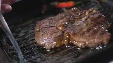 Erkek aşçı, bir parça mermer bifteğin üzerine güzel kokulu yağ döker. Restoranda kızarmış biftek pişirmek. Mutfakta yemek hazırlıyorum. Yemek tarifleri. Gurmeler için lezzetli yemekler. Kapat.