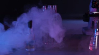 Sıvı nitrojenden çıkan buharın yavaş hareketi. Nitrojen laboratuvar ekipmanlarıyla masaya yayılır. Laboratuvar ekipmanlarının panoramik çekimi. Neon kırmızı ve mavi ışık.