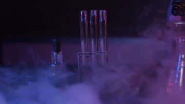 Laboratuvar ekipmanlarının panoramik çekimi. Sıvı nitrojenden çıkan buharın yavaş hareketi. Nitrojen, laboratuvar malzemeleriyle masaya yayılır. Neon kırmızı mavi ışık. Laboratuvarda cam tüpler ve mikroskop.