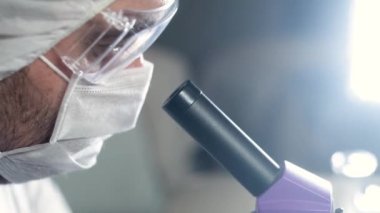 Gözlüklü bilim adamı mikroskoba bakıyor. Kapatın. Mikrobiyoloji veya farmakolojide bilimsel keşifler. Laboratuvar aletleri: mikroskop, test tüpleri. Biyokimya Araştırması