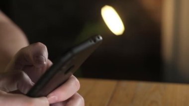 Yetişkin bir adam işyerinde oturuyor ve akıllı telefondan mesaj yazıyor. Cep telefonundaki bir numarayı arayan bir adamın parmaklarının yakın plan görüntüsü. Modern kablosuz teknoloji. Çevrimiçi iş veya alışveriş.