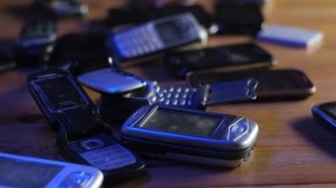 Analog iletişim. Eski, tozlu cep telefonları neon ışıkta masanın üzerinde yatıyor..