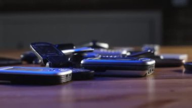 Ofiste analog iletişim. Eski, kırık, çizik ve tozlu cep telefonları neon ışıkta masanın üzerinde duruyor. Modern kablosuz teknoloji. Retro elektroniğin geri dönüşümü. Eski ve telefonun yakın plan görüntüleri..