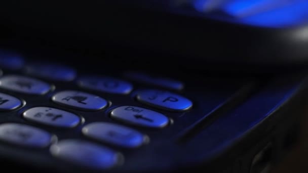 キーボードの古い携帯電話上のボタンのマクロ撮影 古い壊れた傷のついたほこりの多い携帯電話は青いネオンの光のテーブルの上に山にあります オフィスでのアナログ通信 現代の無線技術 — ストック動画