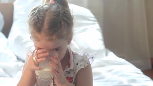 一个白人小女孩坐在床上 喝着新鲜健康的牛奶 儿童及其成长所需的维生素 早餐健康食品 — 图库视频影像