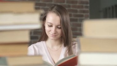 Güzel öğrenci kız kütüphanede kitap yığınlarının arasında oturuyor. Kadın kitap okur ve sayfaları çevirir. Sınav hazırlığı. Öğrenciler evde okuyor. Evde eğitim. Modern eğitim kavramı.