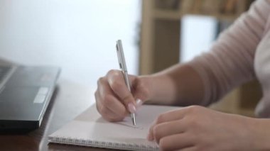 Ofiste dizüstü bilgisayarda çalışan güzel bir genç kız. İş kadını bir not defterine bir kalemle veri yazar ve bilgisayarda metni yazdırır. Evde iş.